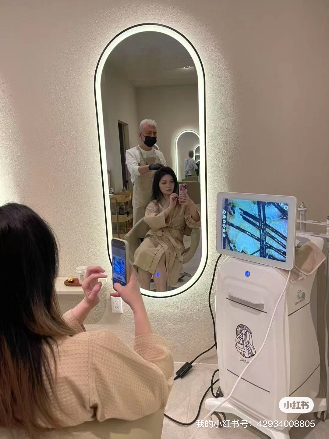 Stylist working on a client's hair at a backlit mirror while a scalp-analysis screen displays the reading