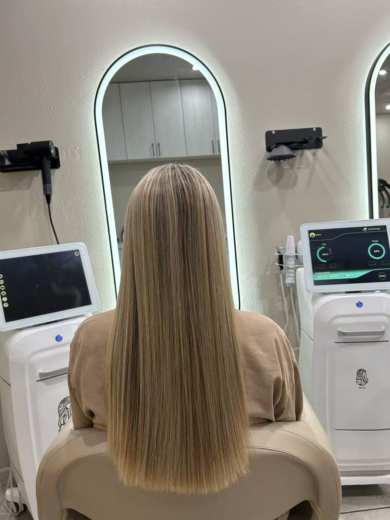 Long blonde hair blown out to a smooth, glossy finish at a backlit arch mirror